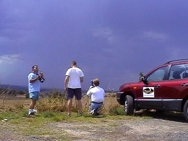 Three storm chasers photographing a dark storm beside the red Thunderbolt Tours vehicle